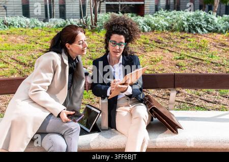 Businesswomen collaborating on documents and digital tablet outdoors Stock Photo