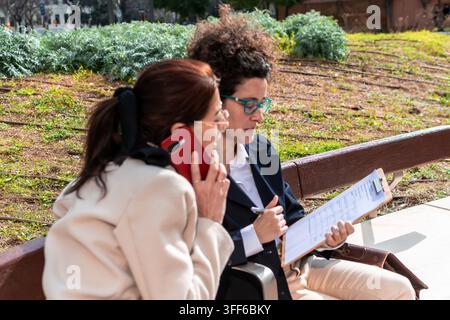 Business women collaborating outdoors discussing work on bench Stock Photo
