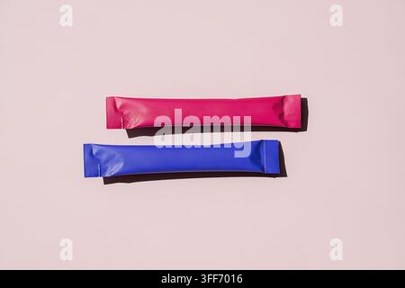 Two blank stick sachet packages in pink and blue on pastel background. Mockup of powder packet, sugar sachet or supplement stick packaging. Minimal pr Stock Photo