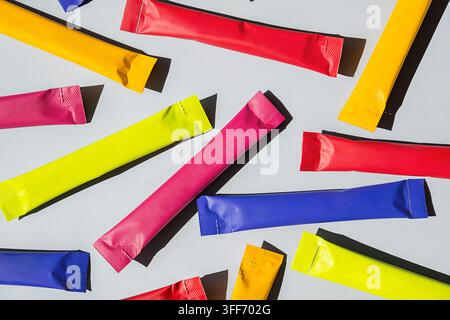 Colorful stick sachet packages scattered on gray background. Bright foil packets for sugar, coffee, powder or snack packaging. Blank packaging design Stock Photo