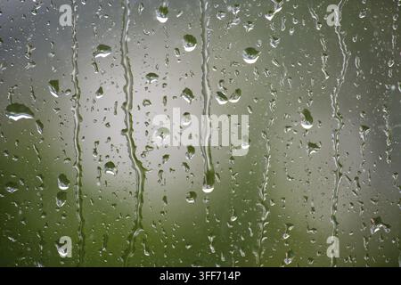 Natural raindrops trickling down a clear glass surface with a soft blurred green garden backdrop creating a soothing atmospheric mood with high detail Stock Photo