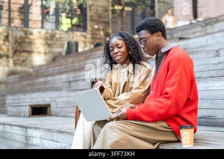 African american students cheerful man and woman sitting talking and enjoying leisure time outdoors. Stock Photo