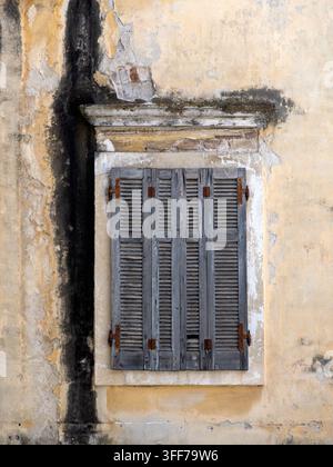 old weathered wooden window with shutters set in worn plastered wall Stock Photo