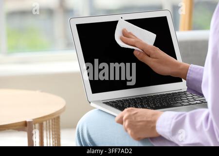 Hygiene and maintenance, person cleaning laptop screen with paper towel for workplace sanitation and digital device care in a bright home office Stock Photo