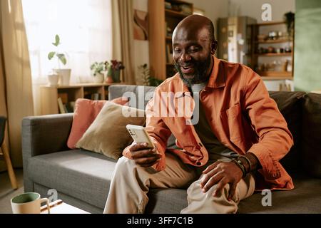 Happy mature African American man holding smartphone for online shopping and browsing seasonal Black Friday discounts. Visual concept suitable for eco Stock Photo