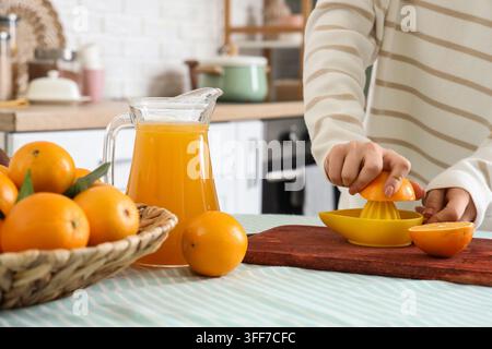 Woman with juicer squeezing fresh oranges in kitchen Stock Photo