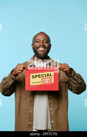 Portrait of smiling middle aged African American man holding discount sign during Black Friday sale promotion, vertical. Commercial concept image suit Stock Photo
