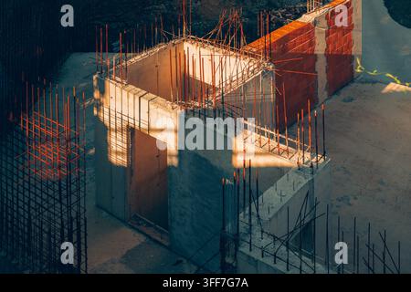 High-angle view of cast concrete walls and exposed steel rebar on a building construction site in warm sunlight. Selective focus. Stock Photo