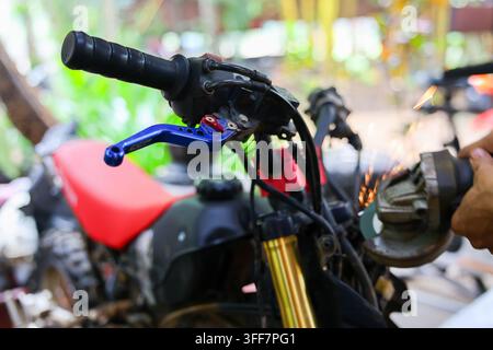 An off road motorcycle handlebar foreground repair outdoors close control lever, mechanic using grinder on brake assembly during maintenance in open w Stock Photo