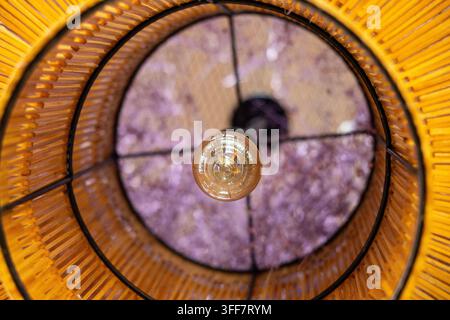 A wicker lampshade pendant light ceiling fixture warm interior design geometric pattern woven rattan lamp shade with glowing bulb and circular texture Stock Photo