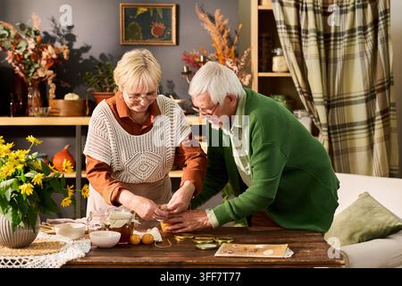 Senior Couple Preparing Homemade Fruit Jam at Table in Kitchen Stock Photo