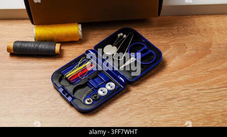 A small, portable sewing kit containing essential mending supplies like colorful threads, needles, a safety pin, and buttons, laid out on a textured w Stock Photo