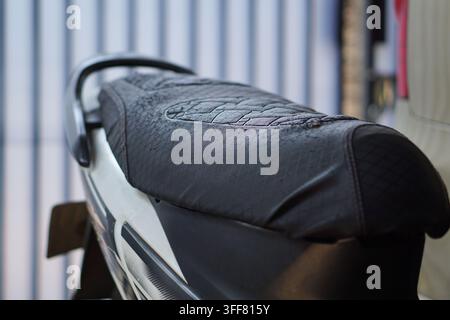 A detailed close-up showing a worn black leather motorcycle seat featuring visible scratches and scuffs in a garage setting. Stock Photo