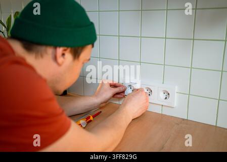 Electrician installing new power outlets in kitchen, connecting wiring and using tools during home renovation for professional repair and maintenance work, close up view of hands and sockets Stock Photo