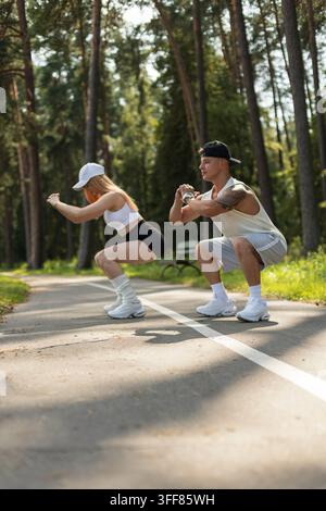 Young athletic couple doing deep squats together during an outdoor fitness training on a park path. Fit man and woman exercising in white sportswear i Stock Photo
