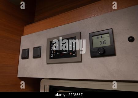 Camper van interior featuring a modern control panel displaying water levels and a screen interface with various illuminated icons, alongside two simp Stock Photo