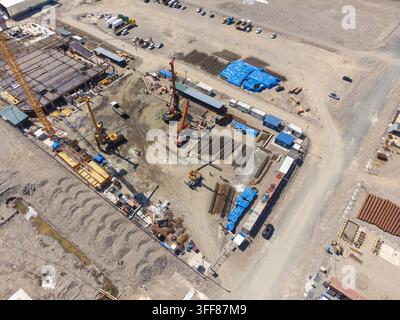 Large construction site from an aerial perspective featuring various heavy machinery. A towering crane. Building foundations Stock Photo