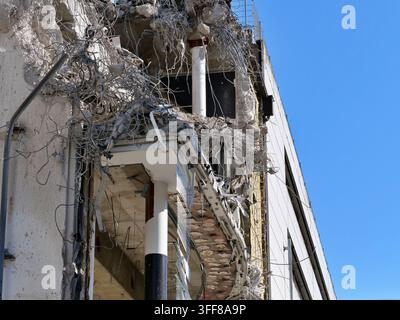 A stark low-angle view showing the severe destruction of a building corner. Exposed steel rebar hangs from shattered concrete balconies and support pi Stock Photo