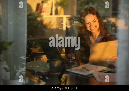 Happy telecommuter working checking documents at home viewed through a window Stock Photo