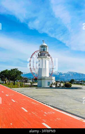White Lighthouse with Ferris wheel and mountain on Black sea coast against blue sky and soft cloud background in Batumi city in Georgia Stock Photo