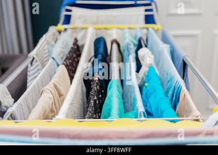 Clean colorful clothes drying naturally on folding laundry rack indoors Stock Photo