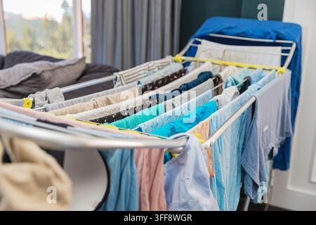 Clean colorful clothes drying naturally on folding laundry rack indoors Stock Photo