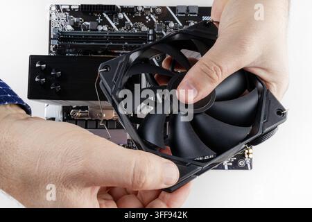 the hands of a man installing a fan on the CPU cooler tower on the motherboard close-up top view Stock Photo