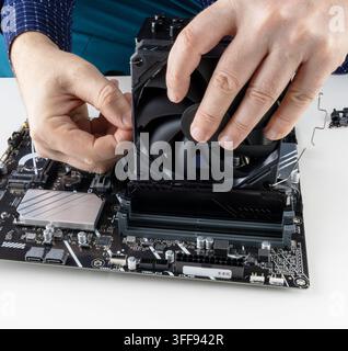 the hands of a man installing a fan on the CPU cooler tower on the motherboard close-up front view Stock Photo