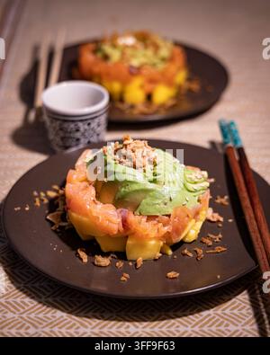 Elegant Japanese-inspired salmon tartare tower layered with diced mango and topped with fanned avocado slices, garnished with crispy onions and sesame Stock Photo