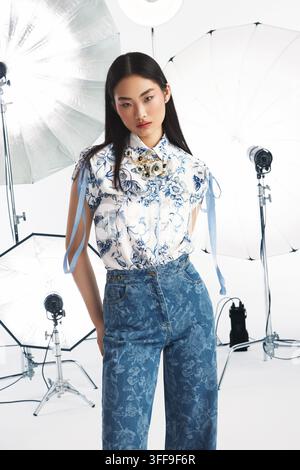 Studio editorial fashion photo of a young Asian model wearing a blue floral crop top paired with wide-leg denim jeans. Stock Photo