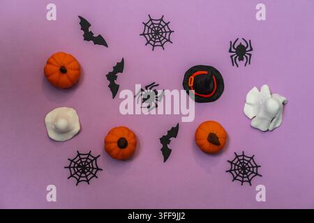 Festive Halloween composition viewed from above, featuring small orange pumpkins, black bats, spiders, spider webs, a witch hat and white ghost figure Stock Photo