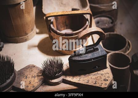 Vintage iron and a small wooden bucket sit among worn tools on a sturdy bench their textures highlighted by gentle light to suggest home industry thri Stock Photo