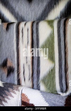 Soft wool blankets with geometric motifs stacked in layers show subtle gray green and earth tones. The tactile fibers and tribal patterns suggest moun Stock Photo