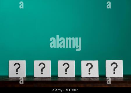 Row of wooden cubes with black question marks printed on faces over bright teal background conceptual metaphor for FAQ choice decision making and prob Stock Photo