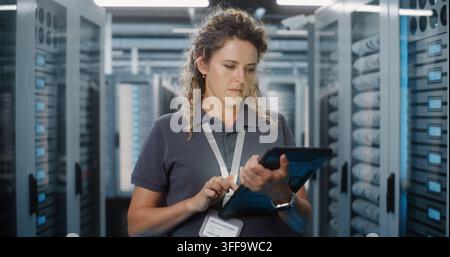 In High Tech Facility, Female Technician Checks Server Telemetry Graphs on Portable Tablet Screen. Cloud Storage Management, Cybersecurity Monitoring Safeguard Critical Enterprise Systems. Portrait. Stock Photo