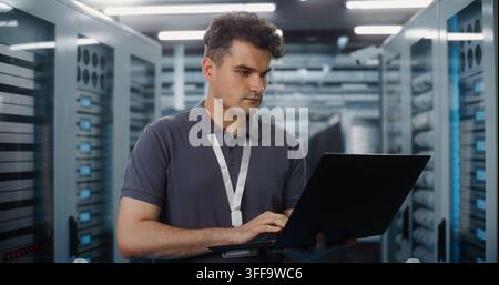 In Data Center, Focused IT Specialist Holds Laptop Inspect Server Racks and Check Network Status. System Diagnostics and Hardware Maintenance Ensure Seamless Cloud Operations. Performance Monitoring. Stock Photo