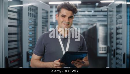 In Modern Data Center, IT Specialist Operates Digital Tablet in Server Room Corridor. Mobile Cloud Management and System Diagnostics Ensure Seamless Server Infrastructure Operation. Portrait. Stock Photo