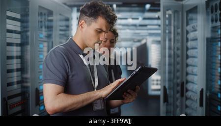 Professional IT Specialist Operates Tablet Computer to Monitor System Status while Female Colleague Inspects Server Rack Hardware. Team Collaboration Ensures Smooth Cloud Infrastructure Performance. Stock Photo
