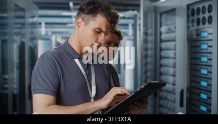 Network Engineer Uses Portable Tablet Screen to Verify System Telemetry, Female Engineer Checks Patch Cables in Server Cabinet. Smart IoT Diagnostics, Hardware Maintenance Secure Enterprise Networks. Stock Photo