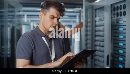 Network Engineer Uses Portable Tablet Screen to Verify System Telemetry, Female Engineer Checks Patch Cables in Server Cabinet. Smart IoT Diagnostics, Hardware Maintenance Secure Enterprise Networks. Stock Photo