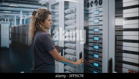 Female Network Administrator Types on Laptop while Analyzing Server Rack Hardware Modules and Cabling. Cybersecurity Management and Cloud Storage Audit Safeguard Critical Enterprise databases. Stock Photo