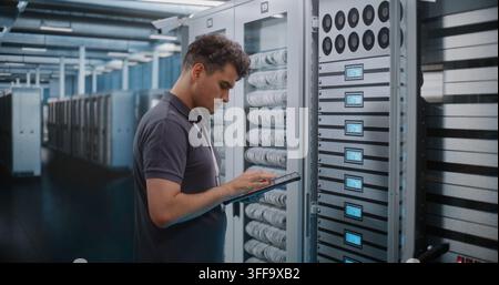 IT Engineer Holds Digital Tablet while Touching and Inspecting Server Rack Modules in Modern Data Center. Routine Hardware Maintenance, Physical Checks Ensure High Availability Server Infrastructure. Stock Photo