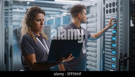 Female IT Specialist and Male Colleague Review System Diagnostics on Laptop Together in Data Center Server Room. Teamwork, Cloud Infrastructure Management Ensure High Availability Server Operations. Stock Photo
