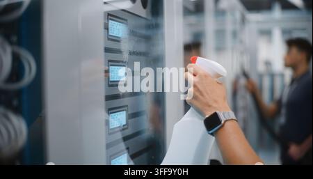 IT Technician Using Cloth to Wipe Server Cabinet Door Near Digital Status Screens, Colleague Vacuums. Physical Maintenance, Dust Removal Ensure Optimal Hardware Performance, Cloud Server Uptime. Stock Photo