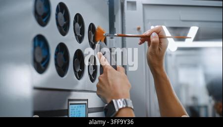Maintenance of Server Rack Fan Assembly. IT Specialist Vacuums Accumulated Dust From Cooling Fan Intakes Near Digital System Monitors, Preventing Thermal Throttling and Enterprise Hardware Damage. Stock Photo
