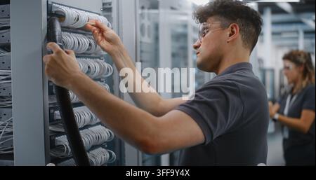 Male Network Technician Uses Soft Brush and Vacuum Nozzle to Clean Dust Off Ethernet Patch Panel Cables Inside Open Server Rack. Hardware Cleaning Prevents Connection Errors and Hardware Failure. Stock Photo