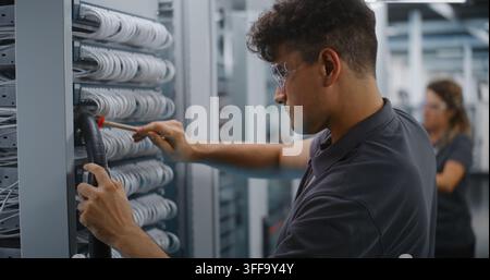 Male Network Technician Uses Soft Brush and Vacuum Nozzle to Clean Dust Off Ethernet Patch Panel Cables Inside Open Server Rack. Hardware Cleaning Prevents Connection Errors and Hardware Failure. Stock Photo