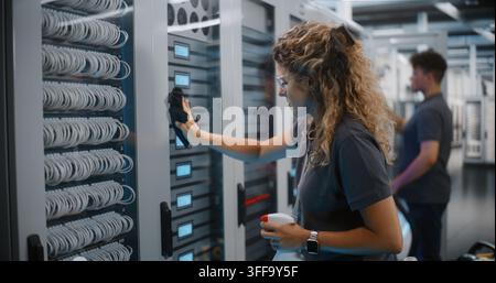 In High Tech Data Center, Female Technician Cleans Server Cabinet Glass With Spray while Male Colleague Vacuums Dust. Professional Facility Maintenance Ensures Reliable Cloud Server Operations. Stock Photo