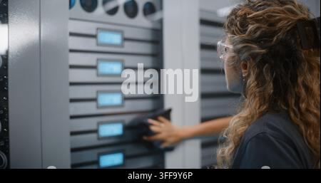 Female IT Specialist Wearing Protective Safety Glasses Wipes Door of Server Rack Cabinet Using Detergent Spray and Cloth. Facility Maintenance and Routine Cleaning Preserve Server Room Hardware. Stock Photo