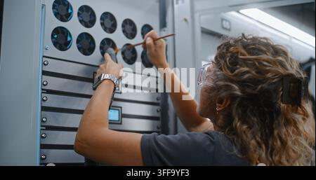 IT Technician Uses Fine Brush and Vacuum Nozzle to Clear Dust From Server Cabinet Cooling Fan Grills. Ventilation Maintenance Ensures Proper Thermal Control and Peak Server Efficiency in Data Centers. Stock Photo